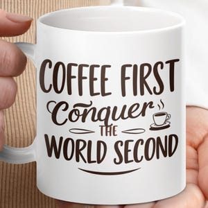 以下が含まれることがあります： 白いセラミックコーヒーマグ。茶色の筆記体で「COFFEE FIRST Conquer THE WORLD SECOND」と書かれています。小さなコーヒーカップのグラフィックが含まれています。マグカップは人が持っています。