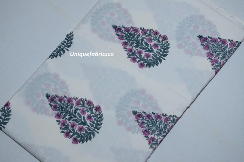 May include: A white fabric featuring a repeating pattern of dark green leaves and pink floral motifs. The text "Uniquefabricsco" is printed in white on the fabric. The material is folded, displaying the botanical print across the surface.