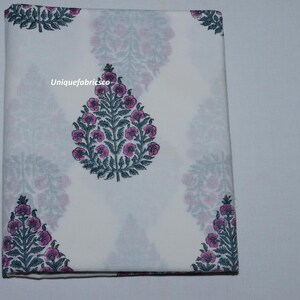 May include: A folded white fabric featuring a repeating pattern of dark green leafy stems with pink floral buds. The text "Uniquefabricsco" is printed in white on the central floral motif. The fabric is rectangular and neatly folded.