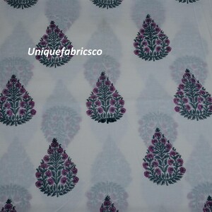 May include: A white fabric featuring a repeating pattern of teardrop-shaped floral motifs in dark green and magenta. Each motif depicts a stylized tree with small circular blossoms. The text "Uniquefabricsco" is printed in white on the fabric.