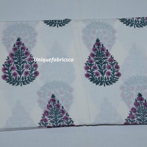 May include: A white fabric featuring a repeating pattern of dark green and pink floral tree motifs. The text "Uniquefabricsco" is printed in white across the center of the fabric. The design consists of symmetrical, stylized botanical shapes.