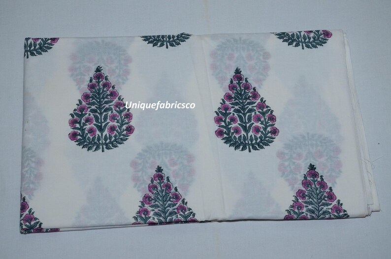 May include: A white fabric featuring a repeating pattern of dark green and pink floral tree motifs. The text "Uniquefabricsco" is printed in white across the center of the fabric. The design consists of symmetrical, stylized botanical shapes.