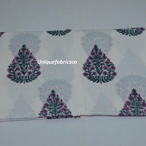May include: A folded piece of white fabric featuring a repeating pattern of dark green and purple floral tree motifs. The text "Uniquefabricsco" is printed in white across the center of the fabric, which displays a symmetrical botanical design.
