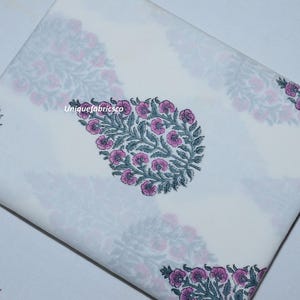 May include: A folded piece of white fabric featuring a repeating pattern of teardrop-shaped floral motifs in muted green and pink. The text "Uniquefabricsco" is printed in small white letters near the center of the fabric surface.