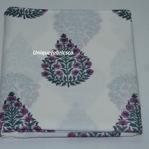 May include: A folded piece of white fabric featuring a repeating pattern of dark green leafy trees with pink flowers. The text "Uniquefabricsco" is printed in white across the center of the fabric. The design consists of symmetrical floral motifs.