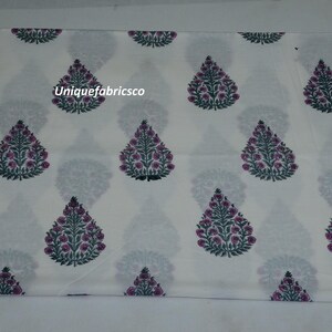 May include: A white fabric featuring a repeating pattern of teardrop-shaped floral motifs in dark green and magenta. The design includes the text Uniquefabricsco printed in white over one of the central floral elements on the textile surface.