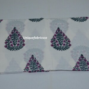 May include: A folded piece of white fabric featuring a repeating pattern of dark green and purple floral tree motifs. The text "Uniquefabricsco" is printed in white across the center of the fabric, which displays a symmetrical botanical design.
