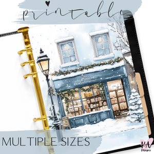 Könnte beinhalten: Druckbarer Planereinsatz mit einer Aquarellillustration eines schneebedeckten Geschäfts. Der Text "Printable" und "Multiple Sizes" ist sichtbar. Das Geschäft hat eine blaue Markise und ist mit festlichem Grün geschmückt, was auf ein Winterthema hindeutet.