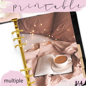 Puede incluir: Un planificador imprimible con un encuadernador dorado y una foto de un libro, una taza de café y luces de cadena en una manta rosa. El texto "printable" y "multiple sizes" es visible en la imagen. El texto "KA Designs" también es visible en la imagen.