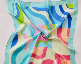 May include: A turquoise blue silk scarf with a colorful abstract design featuring pink, blue, green, and white wavy lines and shapes. The scarf has a white border and a small red signature in the bottom right corner.