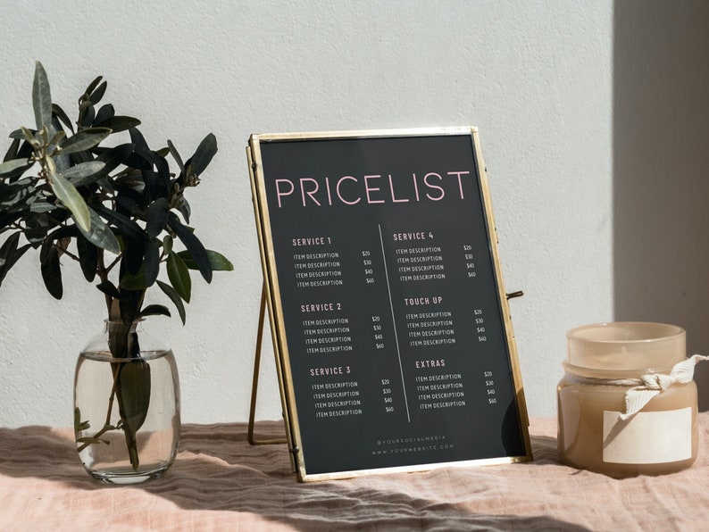 May include: A framed black pricelist with gold trim stands on a pink surface. The text "PRICELIST" is in pink, with service descriptions below. A glass vase with greenery and a small jar with a label are also visible.