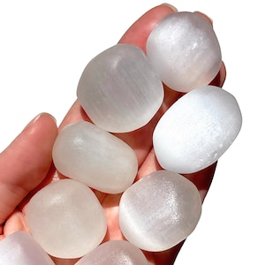 May include: A collection of smooth, white selenite tumbled stones. The stones are various sizes and shapes, with a soft, milky white color.