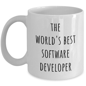 May include: White ceramic mug with a curved handle. The mug features black text that reads "THE WORLD'S BEST SOFTWARE DEVELOPER". The mug is a standard size and shape.