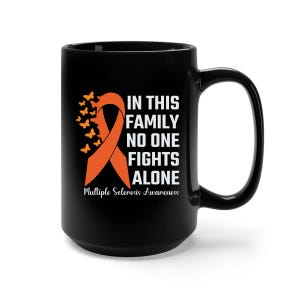 May include: Black ceramic mug with a large handle. The mug features an orange ribbon and butterflies, with the text "IN THIS FAMILY NO ONE FIGHTS ALONE" and "Multiple Sclerosis Awareness" in white.