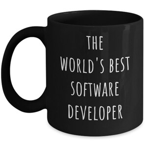 May include: Black ceramic mug with a white handle. The mug features the text "THE WORLD'S BEST SOFTWARE DEVELOPER" in white, centered on the front. The mug is designed for hot beverages.