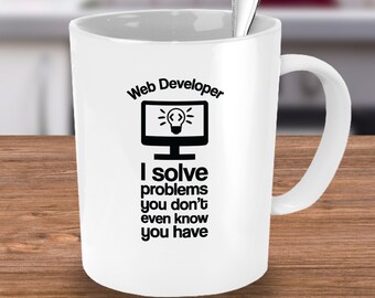 May include: White ceramic mug with a black design that says "Web Developer I solve problems you don't even know you have". The design also includes a computer monitor with a light bulb inside.