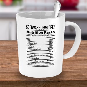 Może przedstawiać: Biały kubek ceramiczny z czarno-białym nadrukiem etykiety wartości odżywczych dla programisty. Etykieta zawiera listę umiejętności, takich jak: adaptacja, kofeina, dbałość o szczeg&oacute;ły, nadgodziny, naprawianie błęd&oacute;w innych, koncentracja i nieodpowiedni humor. Etykieta podaje, że wielkość porcji to 1 pracowity ekspert.