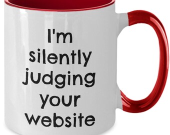 May include: White ceramic coffee mug with a red rim and handle. The mug has black text that reads "I'm silently judging your website."