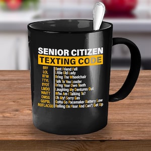 May include: Black coffee mug with a white design that says "Senior Citizen Texting Code" and lists common texting abbreviations and their meanings.
