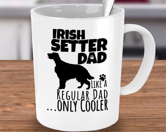Może przedstawiać: Biały ceramiczny kubek z napisem "IRISH SETTER DAD" nad czarną sylwetką psa Irish Setter. Poniżej napis "LIKE A REGULAR DAD...ONLY COOLER". Wewnątrz kubka srebrna łyżeczka.
