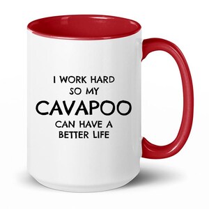 May include: White ceramic coffee mug with a red rim and handle. The mug has black text that reads "I work hard so my Cavapoo can have a better life."