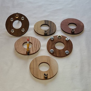 May include: Six wooden rings with different wood grains and brass accents. Each ring has a hole in the center and some have additional holes around the edge.