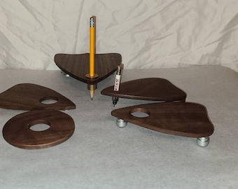 May include: Four wooden coasters shaped like a triangle with rounded edges. The coasters are made of dark wood and have a smooth finish. The coasters are arranged in a pattern on a white surface. A yellow pencil is standing upright in the center of the coasters.