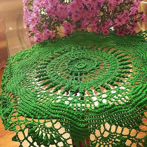 May include: A green crocheted doily with a delicate lace pattern. The doily is round and has a center design with a floral motif.