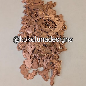 May include: A large pile of copper charms in various shapes and sizes. The charms are all in a copper finish and have a variety of designs, including animals, flowers, and geometric shapes. The charms are perfect for jewelry making, scrapbooking, and other craft projects. @kokolunadesigns