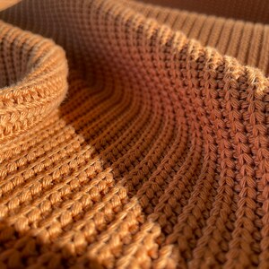 May include: Close-up of a brown knitted fabric with a textured pattern. The fabric is soft and warm, and the texture is visible in the close-up.