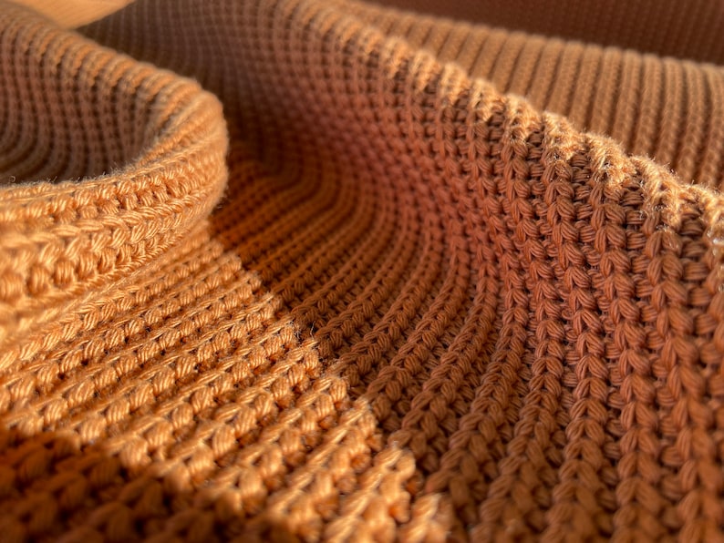 May include: Close-up of a brown knitted fabric with a textured pattern. The fabric is soft and warm, and the texture is visible in the close-up.