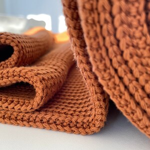 May include: A close-up of a brown knitted throw blanket folded in half. The blanket is made of a soft, textured yarn and has a subtle sheen.