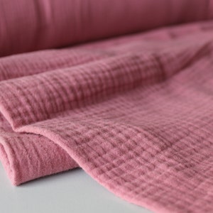 May include: Close-up of a soft, pink, textured fabric. The fabric is folded and has a crinkled appearance.