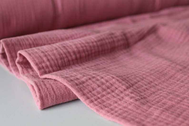 May include: Close-up of a soft, pink, textured fabric. The fabric is folded and has a crinkled appearance.