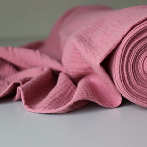 May include: A roll of pink cotton fabric with a textured surface. The fabric is folded and rolled up, showing the layers of the material.
