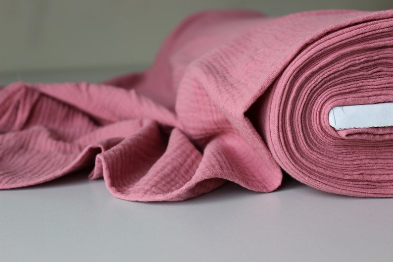 May include: A roll of pink cotton fabric with a textured surface. The fabric is folded and rolled up, showing the layers of the material.