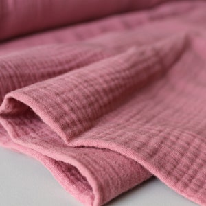 May include: Close-up of a soft, pink, crinkled fabric. The fabric has a textured, gauze-like appearance.