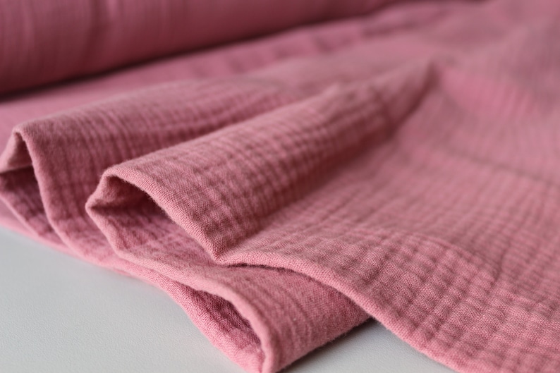 May include: Close-up of a soft, pink, crinkled fabric. The fabric has a textured, gauze-like appearance.