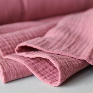 May include: Close-up of a soft, pink fabric folded in layers. The fabric has a textured, crinkled appearance.