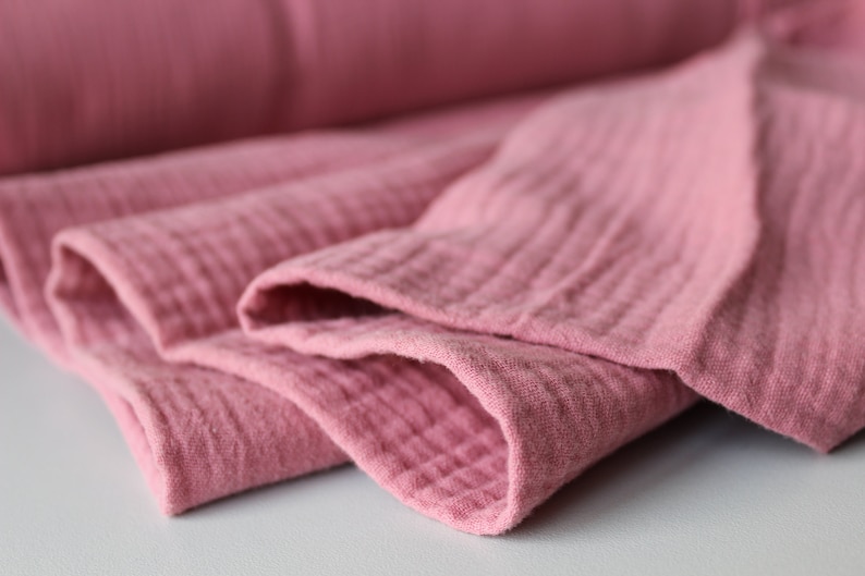 May include: Close-up of a soft, pink fabric folded in layers. The fabric has a textured, crinkled appearance.