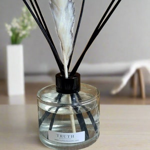 May include: A clear glass aromatherapy diffuser with black reeds and a white feather. The diffuser has a black cap and a label that reads "TRUTH" and "www.truthbodyworks.com". The liquid inside is clear.