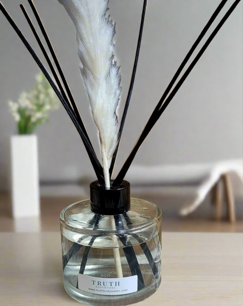 May include: A clear glass aromatherapy diffuser with black reeds and a white feather. The diffuser has a black cap and a label that reads "TRUTH" and "www.truthbodyworks.com". The liquid inside is clear.