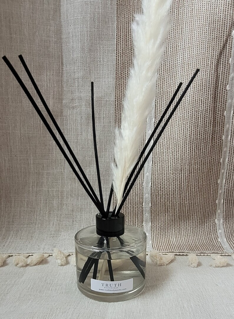 May include: A clear glass diffuser bottle with black reeds and a white fluffy plume. The bottle has a black cap and a label that reads "TRUTH bodyworks". The background is a neutral-toned fabric.