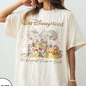May include: Ivory-colored t-shirt featuring a graphic of Disney characters with the text "Walt Disney World" and "The Happiest Place on Earth". The design includes a castle, stars, and various cartoon characters.