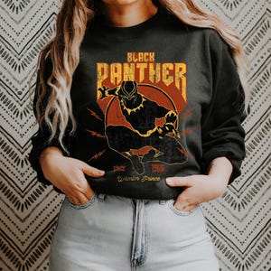 Könnte beinhalten: Schwarzes Sweatshirt mit einer Grafik des Black Panther-Superhelden. Das Design zeigt die Worte "Black Panther", eine Silhouette der Figur und den Text "Since 1966 Warrior Prince".