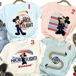 May include: Four t-shirts with travel-themed graphics. One light blue shirt features Mickey Mouse with the text "Have a Nice Flight." Another is pink with Minnie Mouse and "Travel the World." A cream shirt has Mickey and "Have a Nice Flight!" and a light blue shirt has a stylized "S".