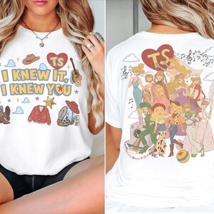 以下が含まれることがあります： フロントに「I KNEW IT, I KNEW YOU」の文字、カウボーイハット、ギター、マイク、ブーツが描かれた白いTシャツ。背面には「TS」と書かれた大きな赤いハート、音符、そしてイラスト化されたキャラクターのグループがプリントされています。