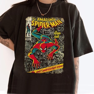 May include: Black t-shirt featuring a vintage comic book cover of Amazing Spider-Man. The comic art shows Spider-Man in a red and blue suit, surrounded by faces. Text includes "Amazing Spider-Man" and "100th Anniversary Issue!"