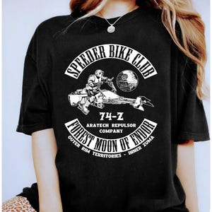 以下が含まれることがあります： 黒いTシャツ。白いグラフィックは、スピーダーバイク、デス・スター、そして「Speeder Bike Club」の文字を描いています。デザインには「74-Z」、「Aratech Repulsor Company」、そして「Forest Moon of Endor」も含まれています。