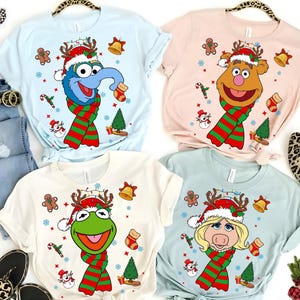 May include: Four short-sleeved t-shirts featuring Muppet characters in festive Christmas attire. Each shirt has a different character, including Gonzo, Fozzie Bear, Kermit the Frog, and Miss Piggy, all wearing Santa hats and scarves.